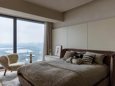 A modern bedroom with a brown velvet bed, a sleek desk, and a large window overlooking a cityscape.