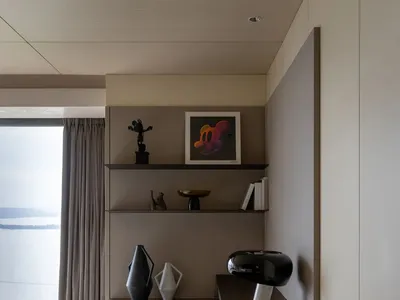 A modern minimalist bedroom featuring a wooden desk, chair, and shelves with decorative items.