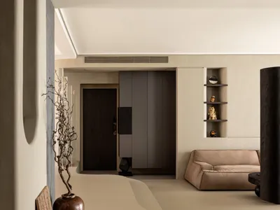 A minimalist living room with concrete walls and floor, featuring a beige couch, wooden accents, and sculptures.