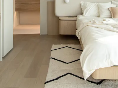 A minimalist bedroom with a white bed and wooden flooring.