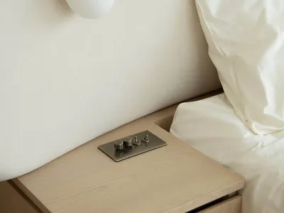 Minimalist bedroom featuring a wooden bedside table with a brushed metal switch panel.