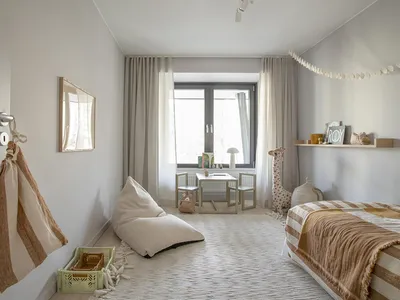 A modern bedroom featuring a bed with striped bedding, a small table and chairs, and a window with curtains.