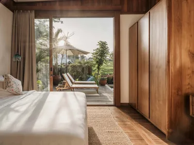 Spacious minimalist bedroom with natural light, wood furnishings, and views of the exterior.