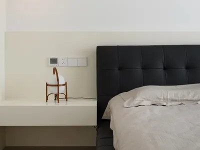 A minimalist bedroom featuring a black leather headboard and light-colored bedding.