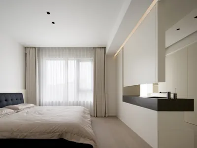 A minimalist bedroom with a large window, white walls, a black bed frame, and wooden flooring.