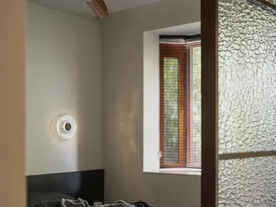 Minimalist bedroom featuring a bed with a grey blanket, dark wood headboard, and a side light fixture on the wall.