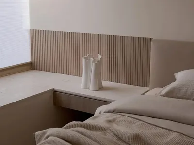 A minimalist bedroom featuring a bed with a wood headboard and beige bedding.