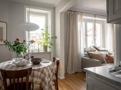 A modern kitchen with a round table covered in a plaid tablecloth, wooden chairs, and a glass vase with flowers.