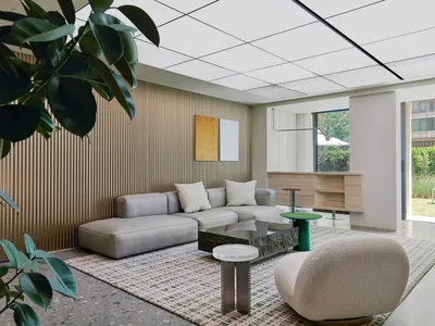 A minimalist living room with concrete and glass elements, featuring a modern sofa, coffee table, and a green stool.