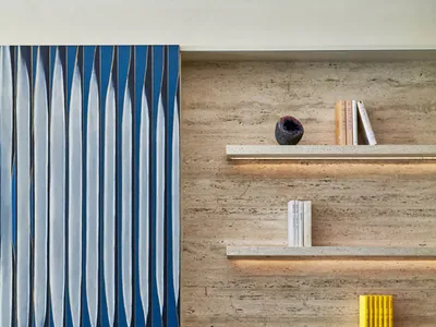 A minimalist living room with a gray upholstered chair, a transparent side table, and a blue and white abstract painting on a