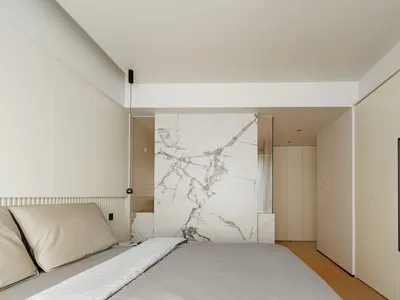 A modern minimalist bedroom with a marble accent wall.