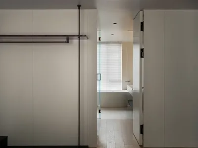 A minimalist bedroom with white walls, a wood floor, and simple furniture