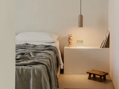 Minimalist bedroom with concrete walls, a wooden bench, and a concrete pendant light hanging above a bed.