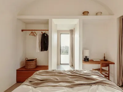 A minimalist bedroom with a wooden bed and wardrobe, featuring a simple design and natural materials, with a door leading to