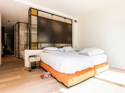 A minimalist bedroom featuring a wooden floor, white walls, and an orange bed frame.
