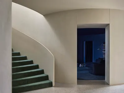 A minimalist living room with concrete walls and green stairs leading to another level.