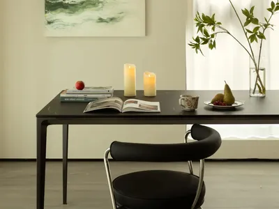 A minimalist home office featuring a black table with candles, an open book, and a chair, with a green abstract painting and