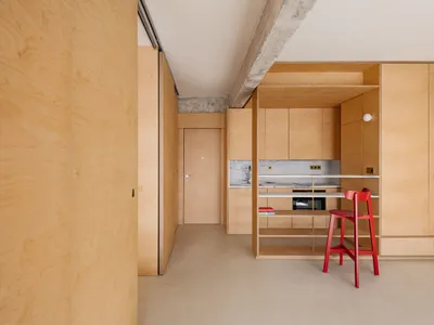 Modern kitchen with wooden cabinets and a red stool.