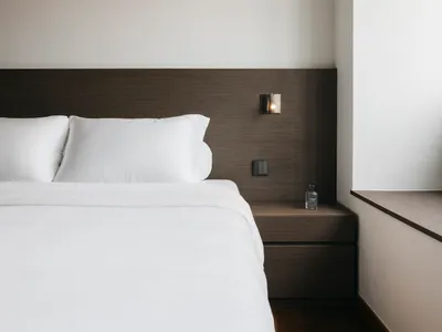 Modern minimalist bedroom featuring white bedding and dark wood headboard and nightstand