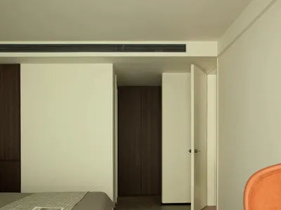 A minimalist bedroom with light wooden flooring, a grey bed, and an orange chair.