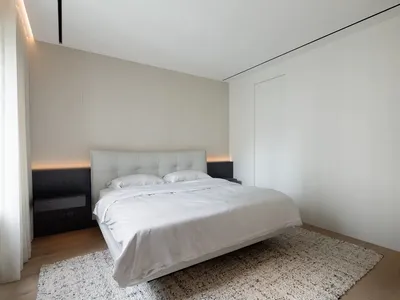 Minimalist bedroom with a white leather platform bed, neutral-toned walls, and a textured rug.