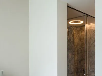 A white minimalist bedroom with a marble shower enclosure and a minimalistic headboard.