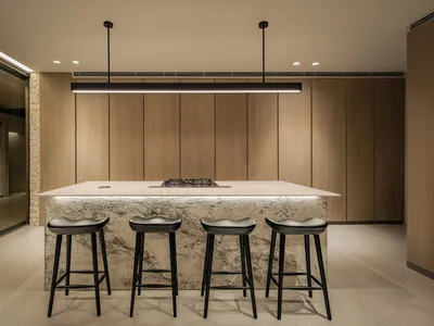 A modern kitchen with wooden cabinets, marble countertops, and black stools.