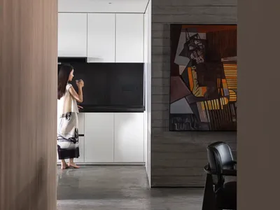 A modern minimalist kitchen with concrete walls, featuring sleek white cabinets and black countertops.