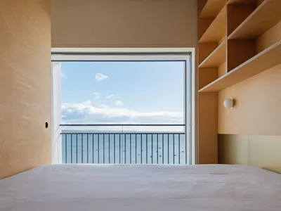 A minimalist bedroom featuring a large window with an ocean view, wood walls, and a bed.