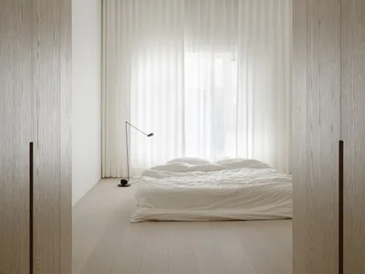A minimalist bedroom with a bed, lamp, and sheer curtains.