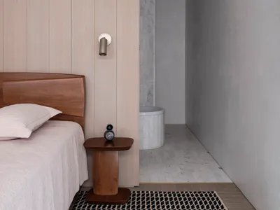 A minimalist bedroom featuring a wooden bed and side table with a modern light fixture.