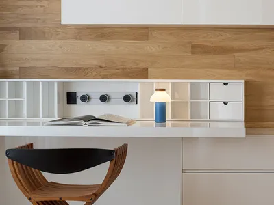 A modern home office featuring a wooden chair and a white desk with a blue lamp on it, set against a wooden wall with built-i