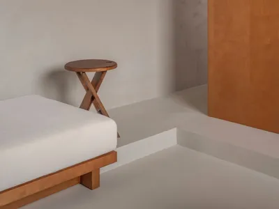 A minimalist bedroom featuring a wooden bed and concrete walls, creating a serene and modern atmosphere.