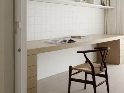 A minimalist home office with a long wooden desk, white bookshelves, and a woven chair.