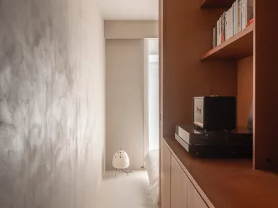 A minimalist bedroom with a wooden shelf, books, and a small table lamp.