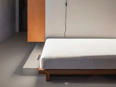 Minimalist bedroom featuring a concrete bed platform, wall-mounted lamp, and wooden accents.