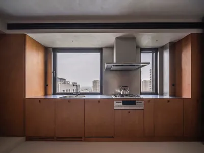 A modern minimalist kitchen with wooden cabinetry and a large window overlooking urban skyline.