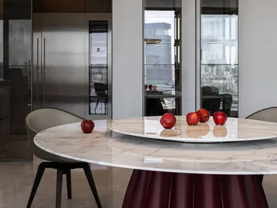 A modern kitchen featuring a round marble table with apples and a contemporary pendant light fixture.