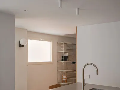 A photograph of a modern minimalist kitchen featuring a concrete countertop with a glass cylinder light, a bread loaf, and a