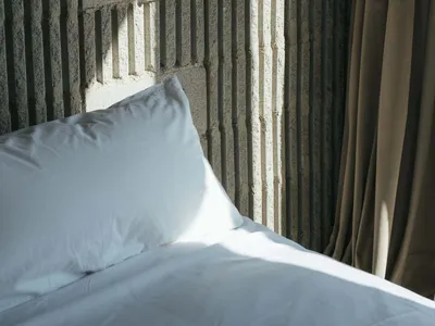 A minimalist bedroom with a concrete textured wall and a white pillow on a bed.