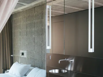 Modern minimalist bedroom featuring a metal vanity sink, white linens, and a textured wall behind the bed.