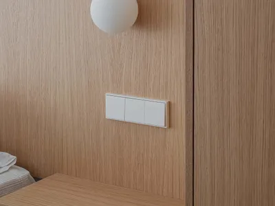 A modern oak bedside table with a white spherical lamp and minimalist wall switches.