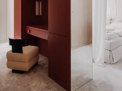 A modern bedroom featuring a dressing table with red cabinets and a beige upholstered stool.