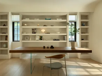 A modern home office with a wooden desk, glass table legs, and built-in shelves.