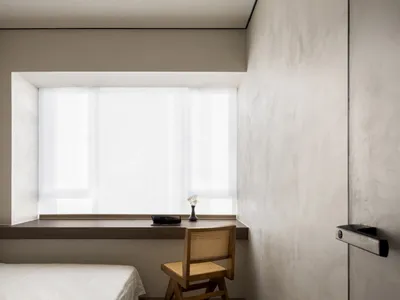 A minimalist bedroom with a bed, chair, and window.