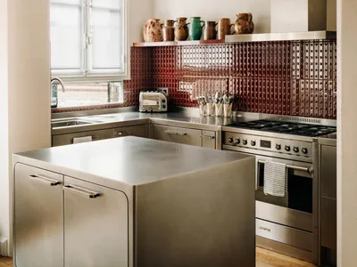 A modern kitchen with a metal island, stainless steel appliances, and a red-tile backsplash displaying a variety of ceramic v