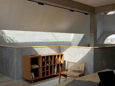 Modern minimalist bedroom featuring a concrete ceiling with a large circular cutout, natural light, and simple furniture.