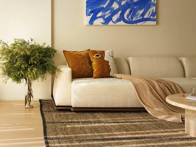 A minimalist living room featuring a white sofa with blue and white abstract art above, a wooden coffee table, and a woven ru