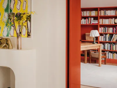 Modern home office with red-painted wooden door and yellow-green abstract artwork hanging on white wall.