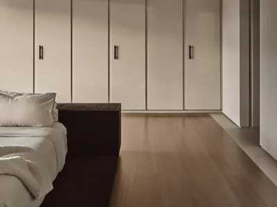 A minimalist bedroom featuring white paneling and wooden floors, with a sleek bed and minimalistic decor.